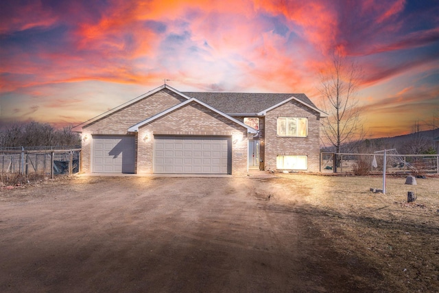 tri-level home featuring fence, an attached garage, a shingled roof, brick siding, and dirt driveway