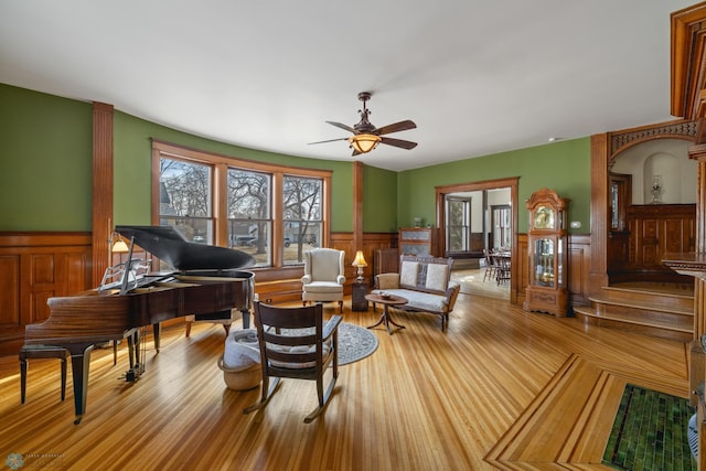 living area with a ceiling fan, wood finished floors, and wainscoting