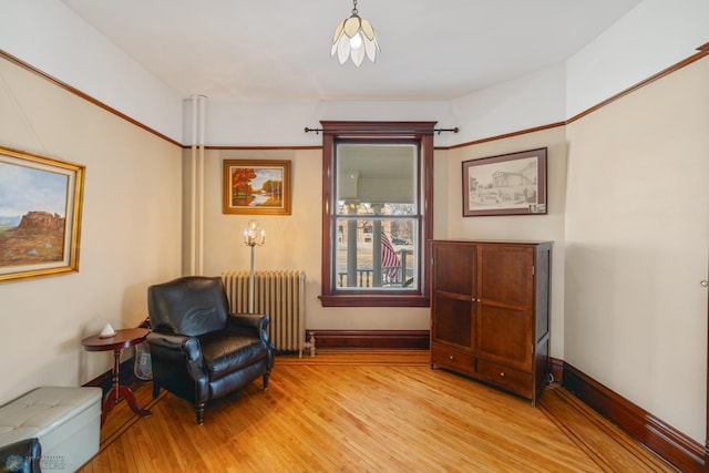 sitting room featuring baseboards, light wood finished floors, and radiator