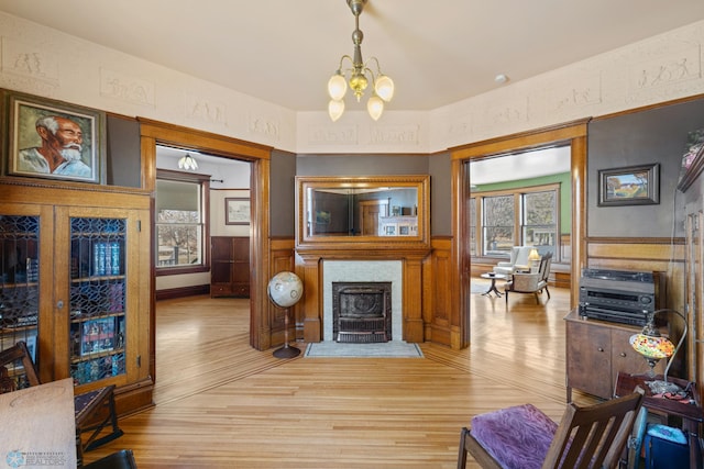 living area featuring wainscoting, a notable chandelier, light wood-type flooring, and a fireplace