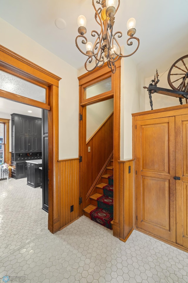 staircase with an inviting chandelier, wood walls, and wainscoting