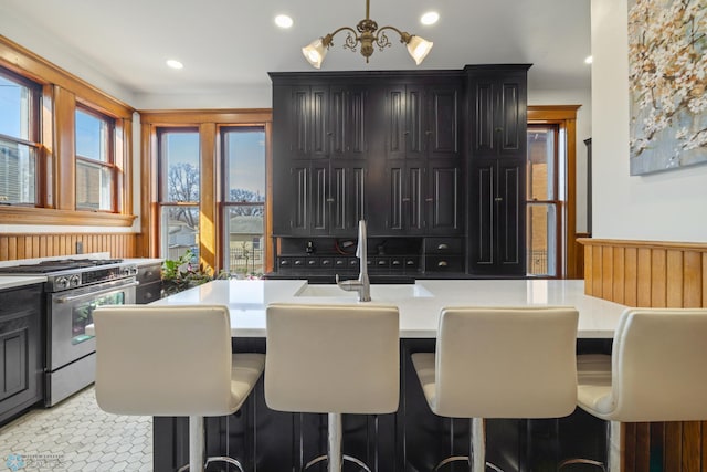 kitchen with light countertops, a sink, a breakfast bar area, dark cabinetry, and gas stove