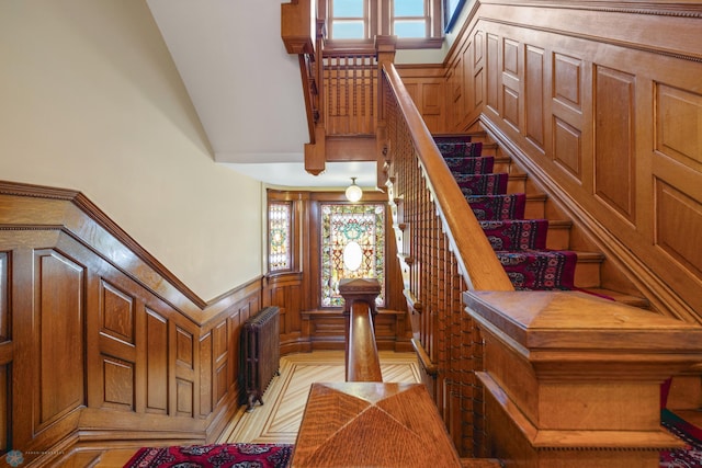 staircase featuring radiator heating unit, a wainscoted wall, and high vaulted ceiling