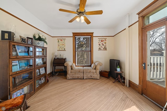 living area with baseboards, a ceiling fan, light wood-style floors, and a healthy amount of sunlight