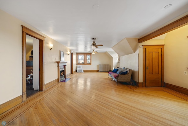 bonus room with a ceiling fan, light wood-style flooring, baseboards, and a lit fireplace