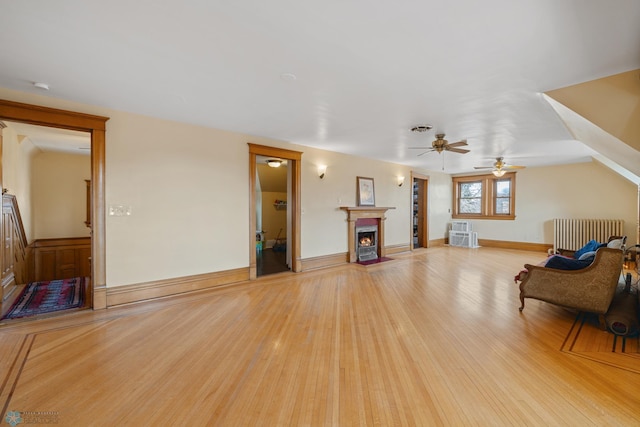 living area featuring light wood-style flooring, baseboards, ceiling fan, radiator heating unit, and a lit fireplace