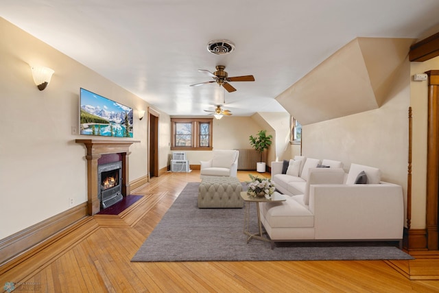 living area with a warm lit fireplace, baseboards, visible vents, ceiling fan, and hardwood / wood-style floors