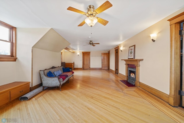 unfurnished room with a fireplace with flush hearth, ceiling fan, baseboards, and light wood-type flooring