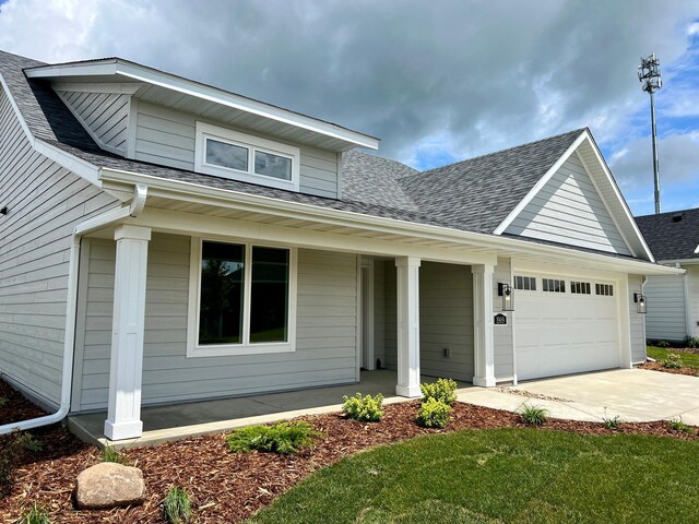 view of front of property featuring driveway, a shingled roof, covered porch, and an attached garage