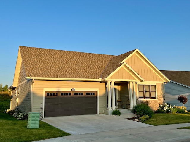 craftsman house featuring stone siding, a garage, a front lawn, roof with shingles, and driveway