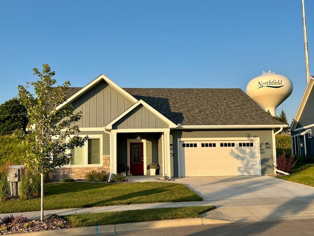 view of front of house featuring driveway, a front yard, stone siding, an attached garage, and board and batten siding
