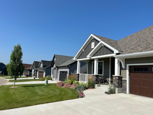 craftsman-style house featuring driveway, a front yard, stone siding, an attached garage, and board and batten siding