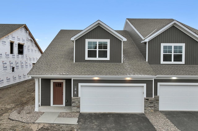 view of front facade with stone siding, driveway, and a shingled roof