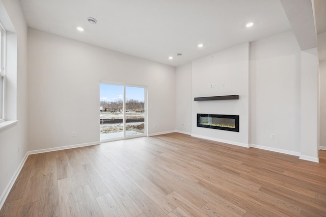 unfurnished living room with recessed lighting, a glass covered fireplace, and light wood finished floors