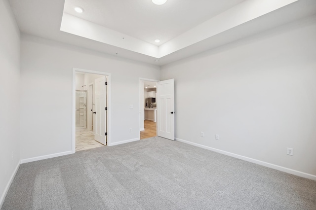 unfurnished bedroom featuring light carpet, baseboards, ensuite bathroom, recessed lighting, and a tray ceiling
