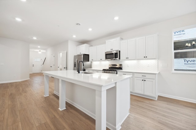kitchen featuring decorative backsplash, a center island with sink, a sink, stainless steel appliances, and white cabinetry
