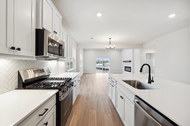 kitchen featuring white cabinets, a sink, light wood-style flooring, stainless steel appliances, and backsplash