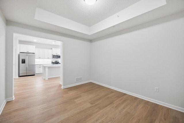 empty room with baseboards, a tray ceiling, light wood finished floors, and visible vents