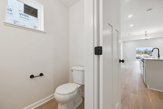 bathroom featuring wood finished floors, toilet, baseboards, a chandelier, and a sink