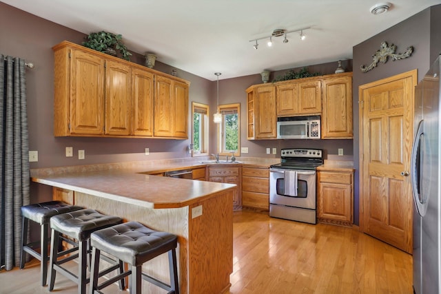 6875 148th Ln NW, Ramsey, MN 55303 - kitchen with stainless steel appliances, a peninsula, a sink, a kitchen breakfast bar, and light wood-style flooring