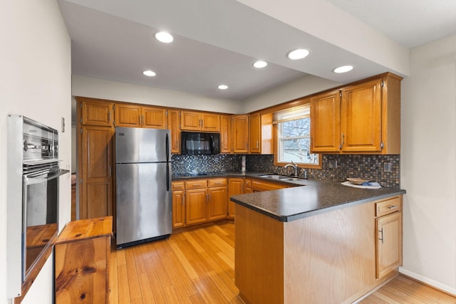 kitchen featuring freestanding refrigerator, light wood-style floors, a sink, black microwave, and a peninsula