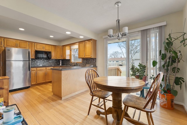 kitchen featuring decorative backsplash, light wood-type flooring, black microwave, dark countertops, and freestanding refrigerator