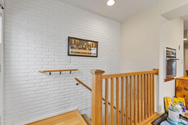 stairs featuring recessed lighting, wood finished floors, and brick wall