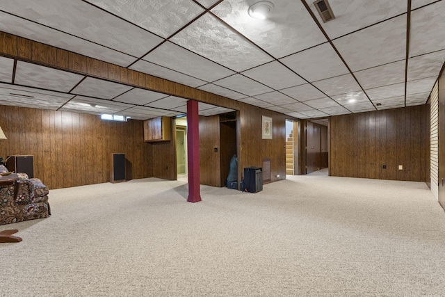 basement featuring wooden walls, a paneled ceiling, and carpet floors