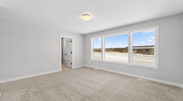 empty room with baseboards, visible vents, and light carpet