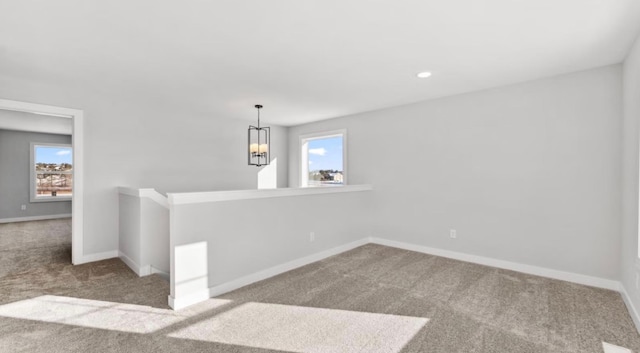 carpeted spare room featuring baseboards, a notable chandelier, and a wealth of natural light