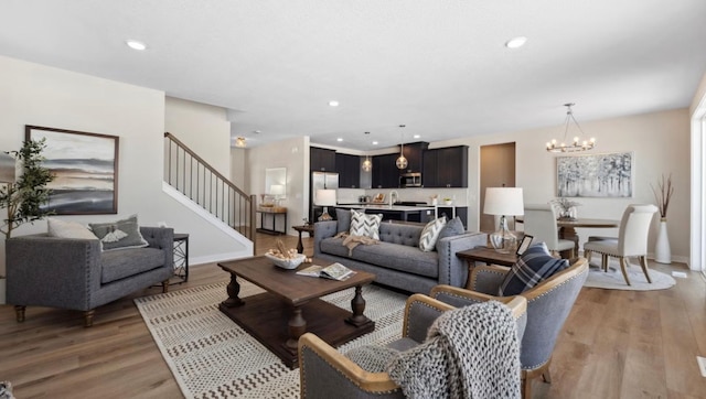 living room featuring baseboards, an inviting chandelier, light wood-style flooring, and stairway