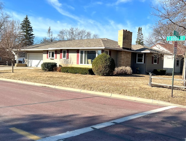 ranch-style home with a chimney, a garage, and roof with shingles