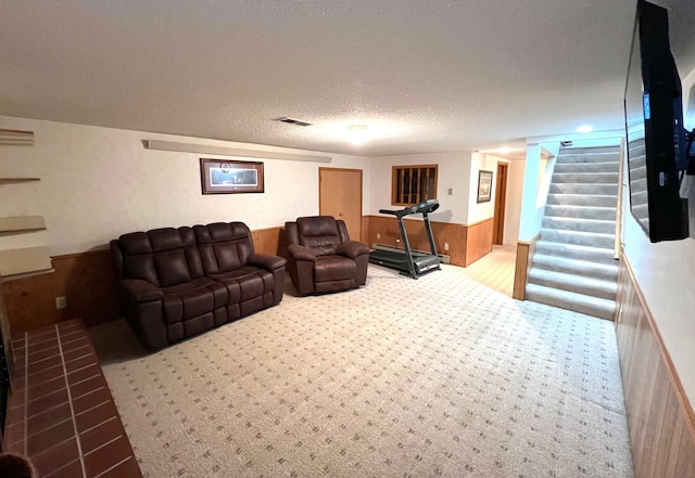 living area featuring stairway, carpet, a textured ceiling, visible vents, and wainscoting