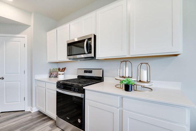 kitchen with appliances with stainless steel finishes, white cabinets, light wood finished floors, and light countertops