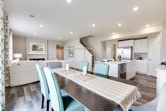 dining space with dark wood-type flooring, recessed lighting, a fireplace, and stairs