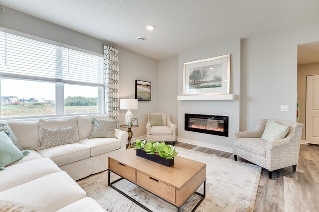 living area featuring light wood-style flooring, recessed lighting, a textured ceiling, baseboards, and a glass covered fireplace