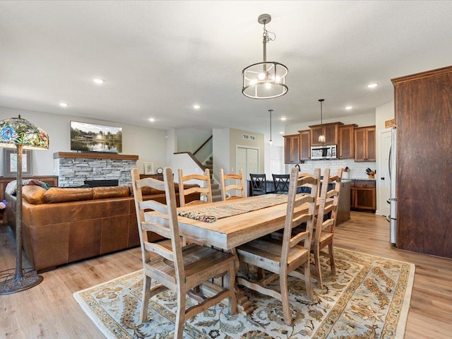 dining room featuring a fireplace, light wood-type flooring, recessed lighting, and stairway