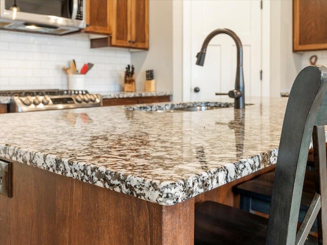 kitchen featuring stainless steel microwave, tasteful backsplash, brown cabinets, range, and a breakfast bar area
