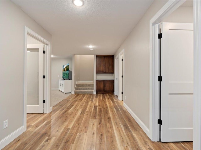 corridor with light wood-type flooring, baseboards, stairs, and recessed lighting