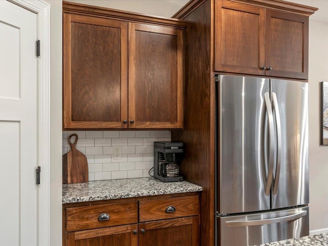 kitchen with freestanding refrigerator, decorative backsplash, and light stone countertops