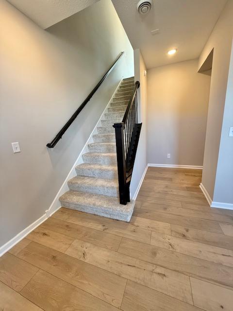 staircase with wood-type flooring, visible vents, and baseboards