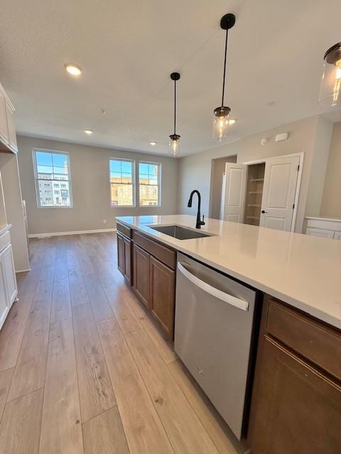 kitchen with stainless steel dishwasher, light wood-style flooring, a sink, light countertops, and hanging light fixtures