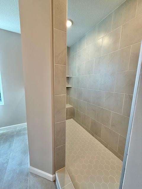 full bath with baseboards, tile patterned flooring, a textured ceiling, and a tile shower