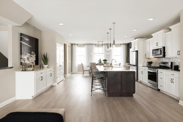 kitchen with light wood-style flooring, a breakfast bar, a kitchen island with sink, a sink, and stainless steel appliances