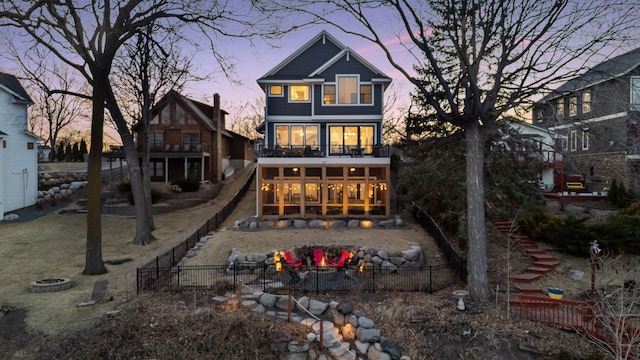 back of house at dusk with a sunroom, stairway, a balcony, a fenced backyard, and an outdoor fire pit