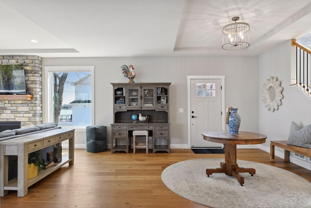 foyer with stairs, baseboards, light wood-style floors, a raised ceiling, and a notable chandelier