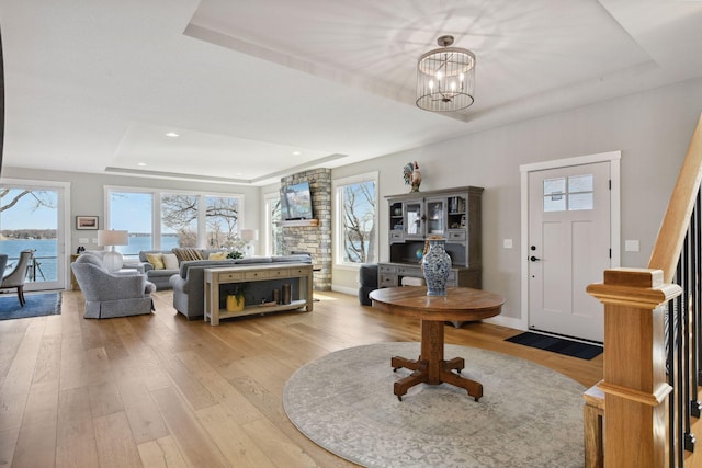 foyer entrance featuring a tray ceiling, a chandelier, a healthy amount of sunlight, and light wood-type flooring