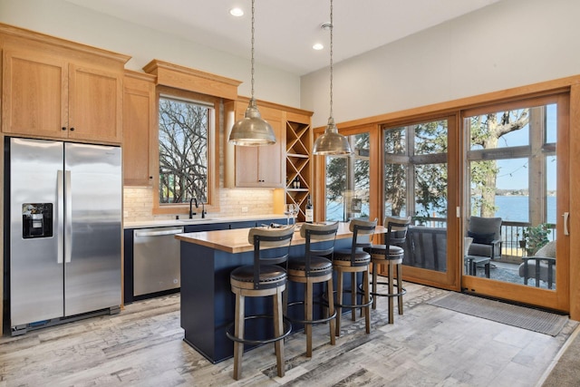 kitchen with pendant lighting, a kitchen island, a sink, light wood-style flooring, and stainless steel appliances