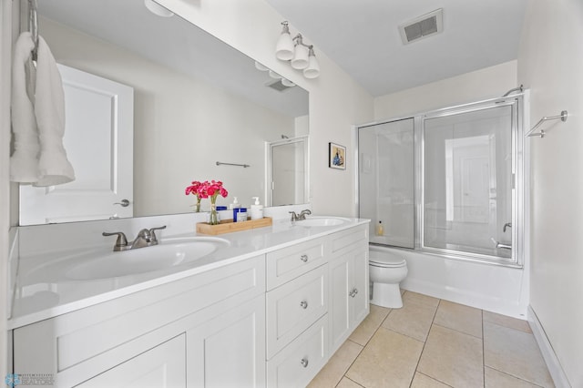full bathroom with double vanity, toilet, bath / shower combo with glass door, tile patterned floors, and baseboards