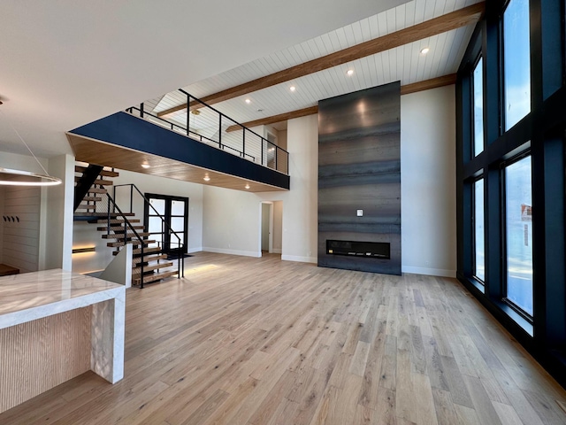 unfurnished living room with stairs, a high ceiling, a healthy amount of sunlight, and wood finished floors